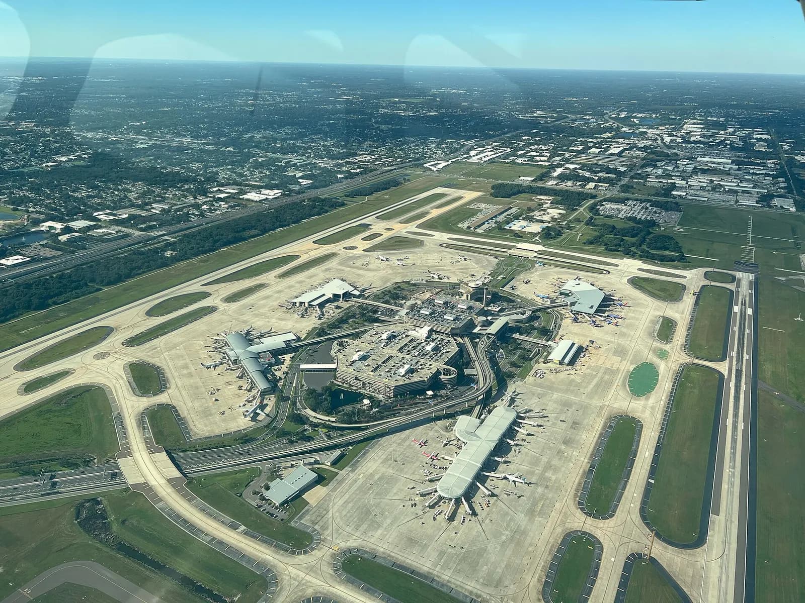 Aerial view from above showing Tampa International Airport's four satellite terminal buildings—Airsides A, C, E, and F—arranged around runways and taxiways.