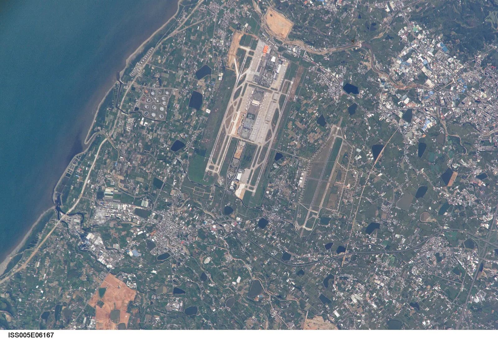 A satellite aerial view shows Taoyuan International Airport's parallel runways, terminal complexes, and surrounding Taoyuan area.