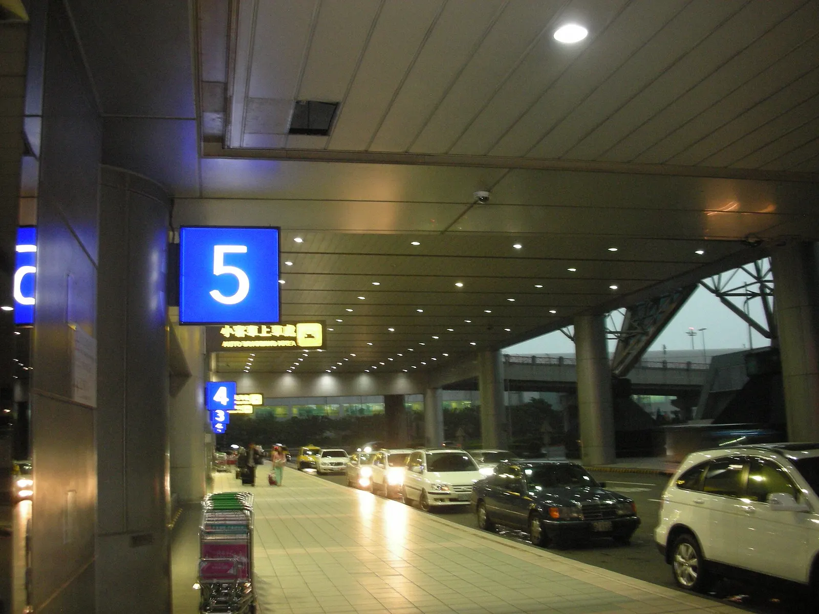 The curbside pickup and drop-off lanes outside Terminal 2 at night, with vehicles, terminal lighting, and the building facade visible.
