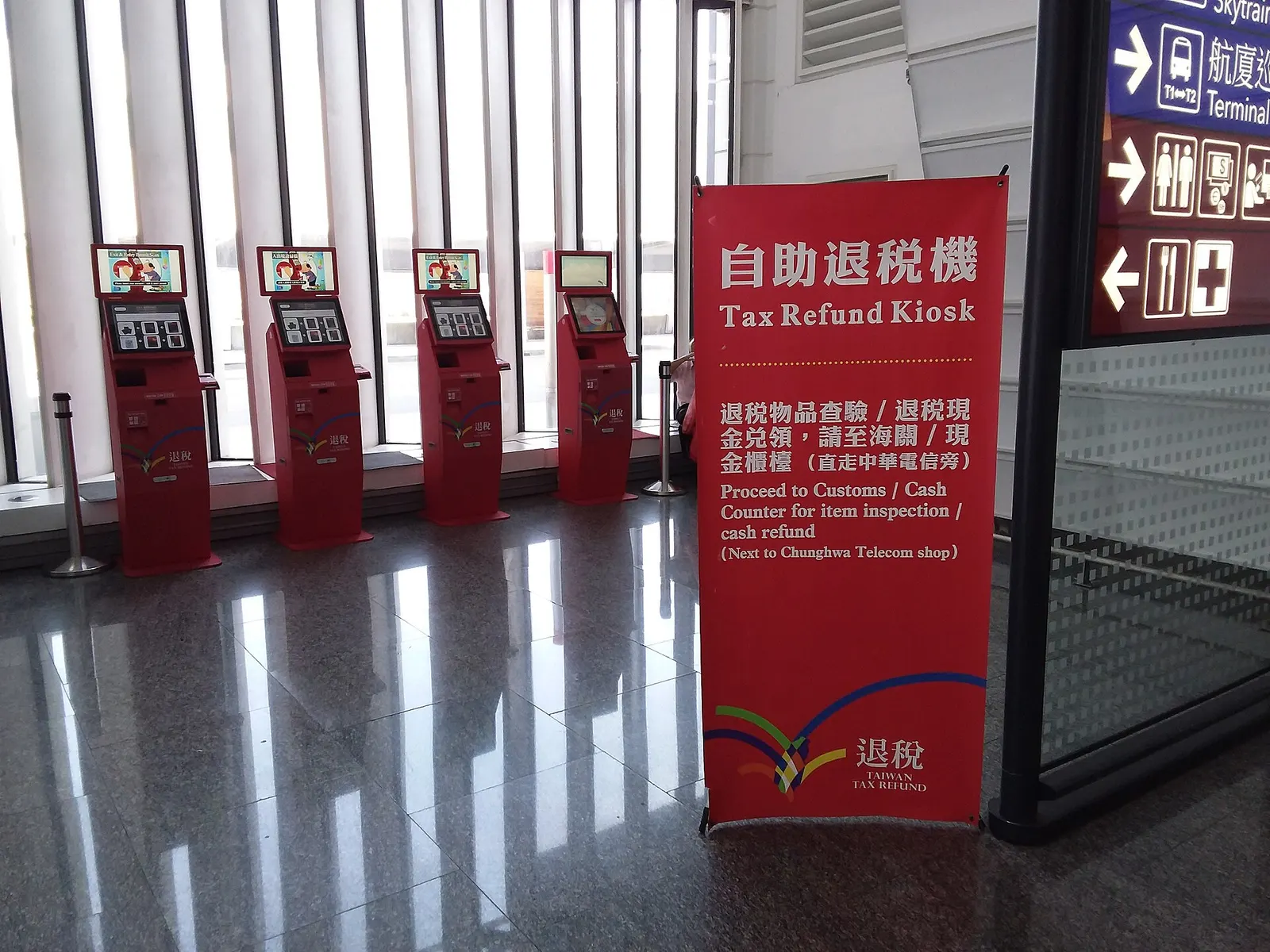 Tax-refund kiosks stand in a row along a wall in Terminal 1, with instructions and screens for departing shoppers.