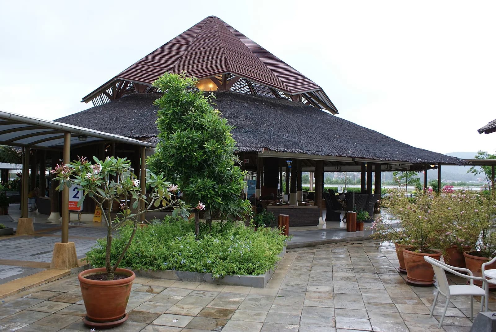 Open-air departure gate pavilion at Samui Airport with thatched roof and tropical landscaping
