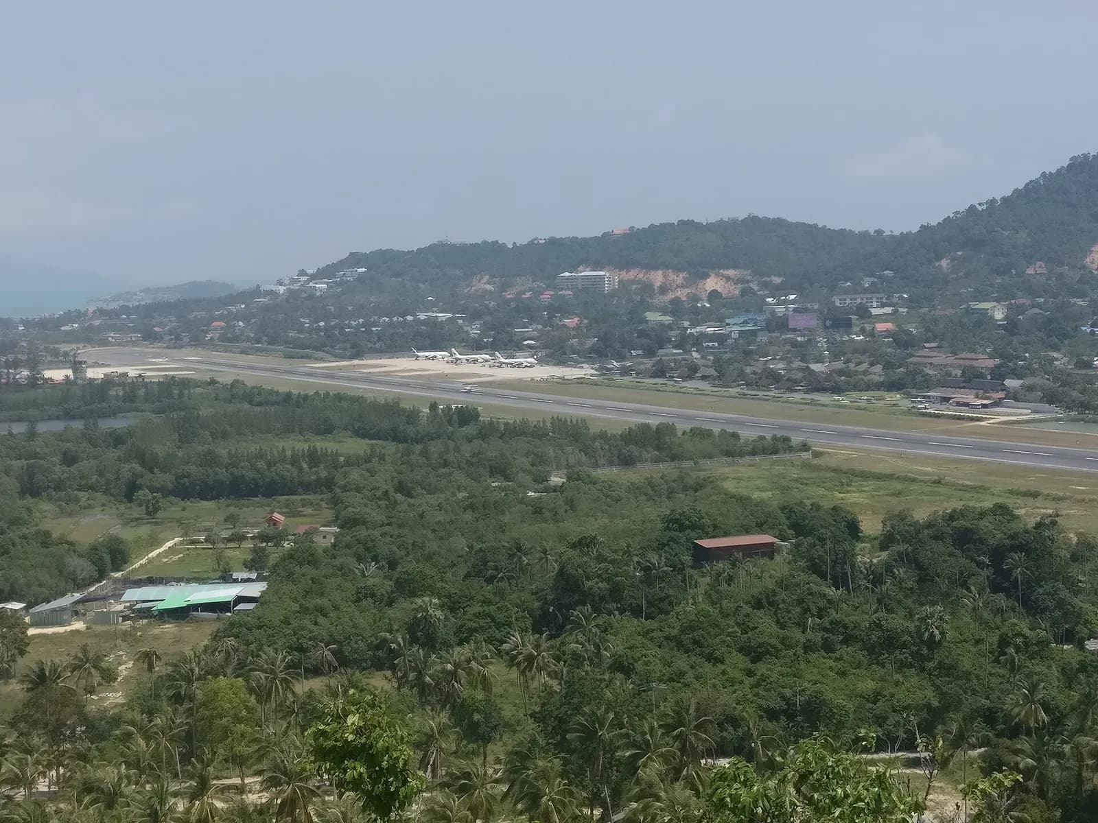Aerial view of Ko Samui Airport runway and open-air terminal campus among coconut palms