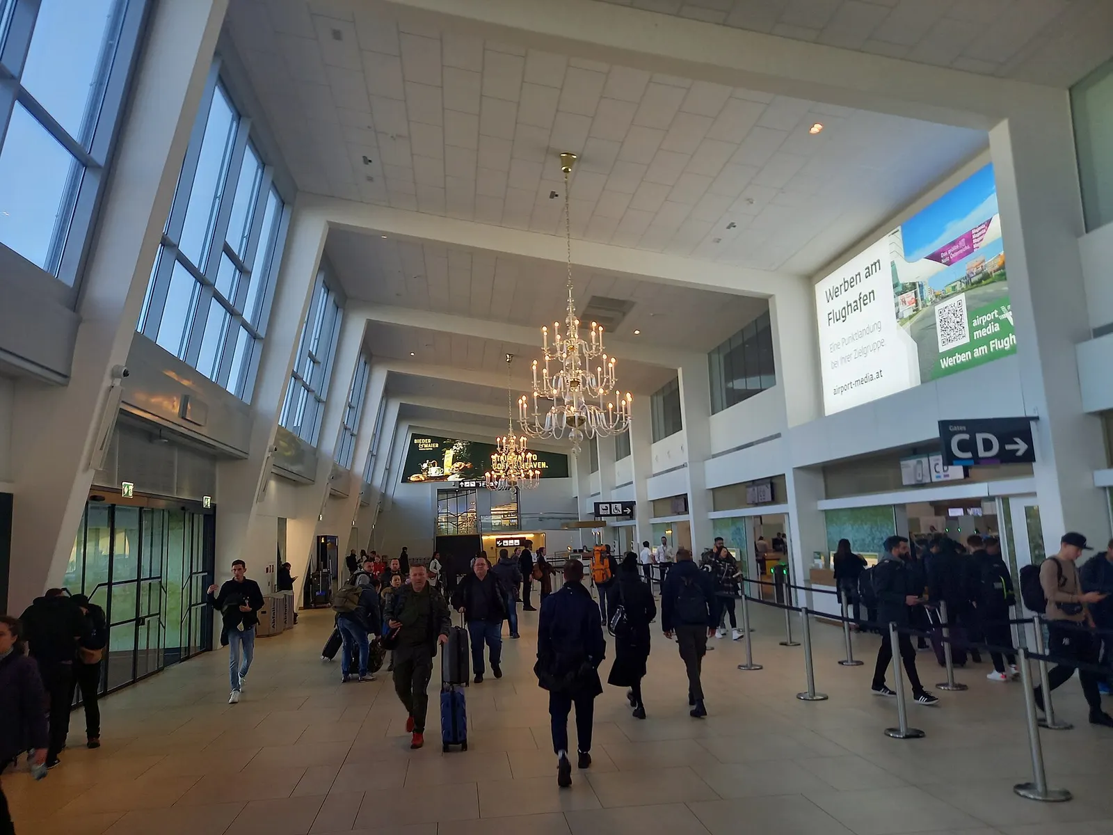 A central security screening area with multiple lanes, conveyor belts, x-ray machines, and travelers removing items from carry-on bags.