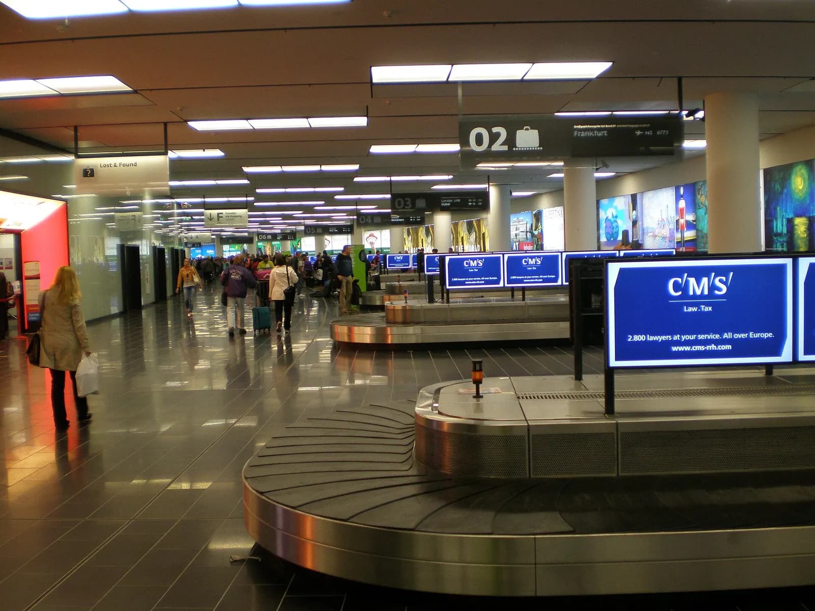 The central baggage claim hall with luggage carousels, overhead flight-information screens, and travelers waiting for bags.
