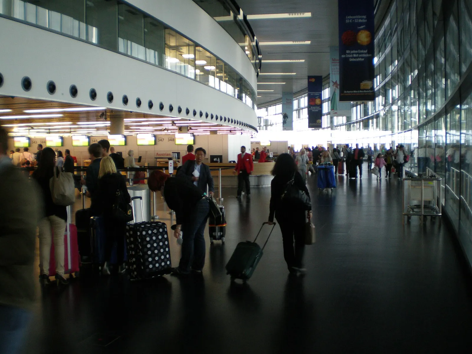 The spacious Check-In 3 hall with airline counters, overhead departure screens, and passengers queuing with luggage carts.