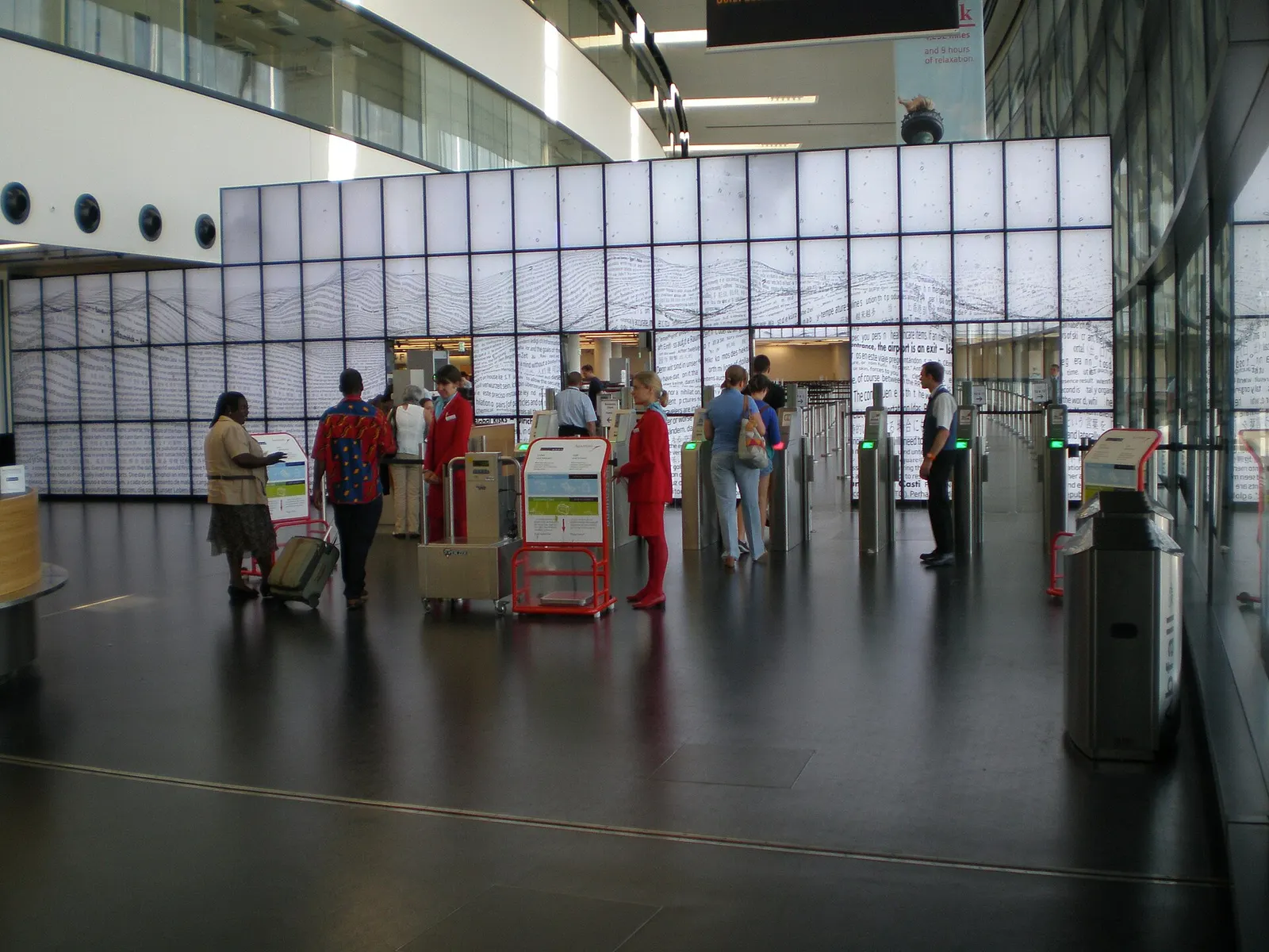 Passengers pass through a boarding-pass control corridor bordered by a large digital art wall displaying colorful animated patterns.