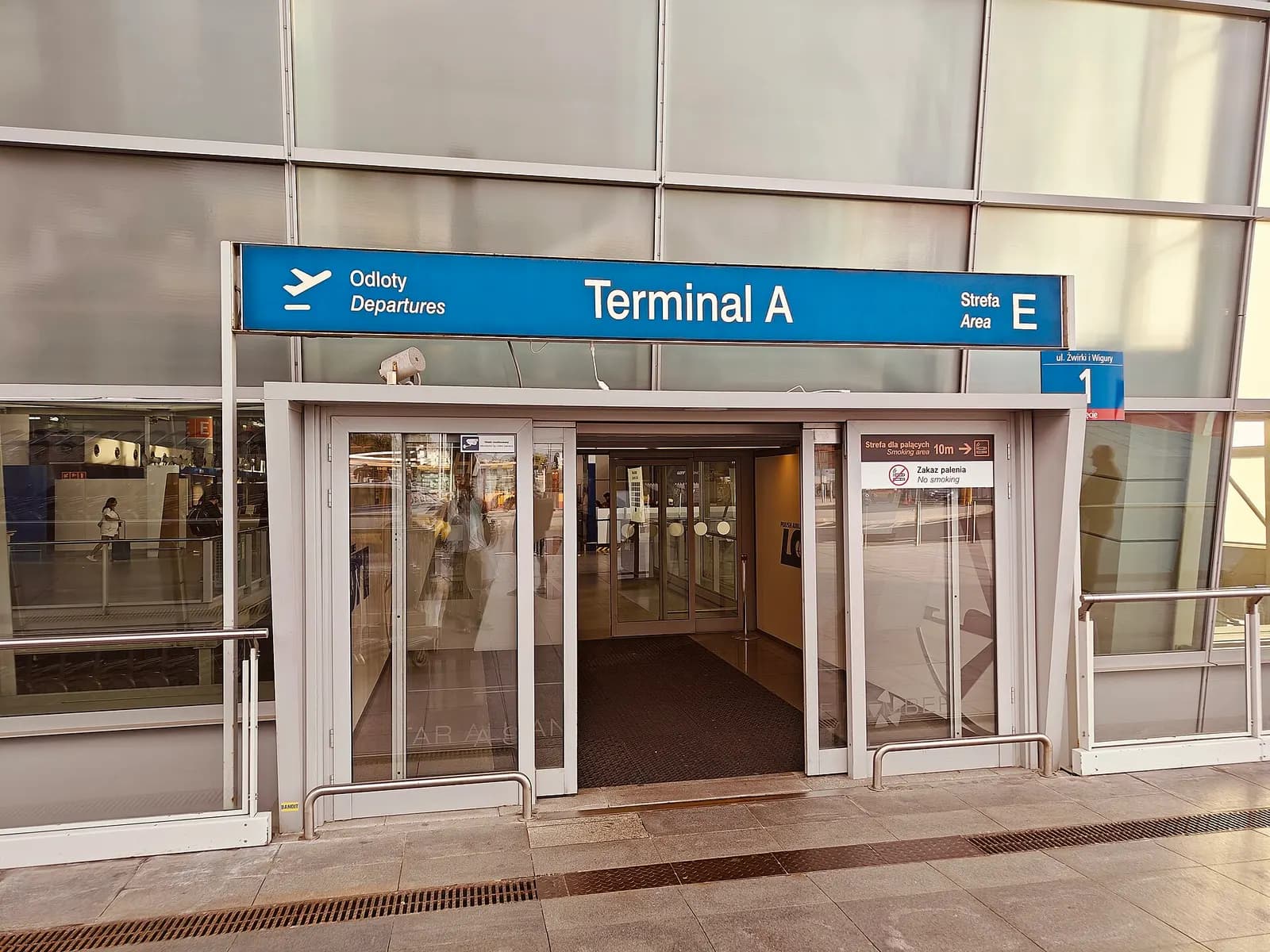 The road-level entrance to Terminal A with glass doors, overhead signage, and drop-off lanes for cars and taxis.