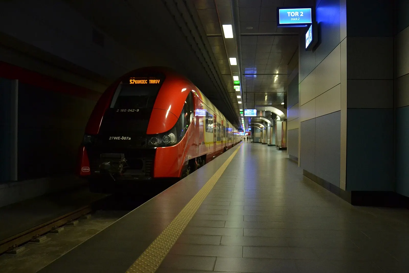 A modern SKM suburban train stopped at the Warszawa Lotnisko Chopina platform beside the station canopy.