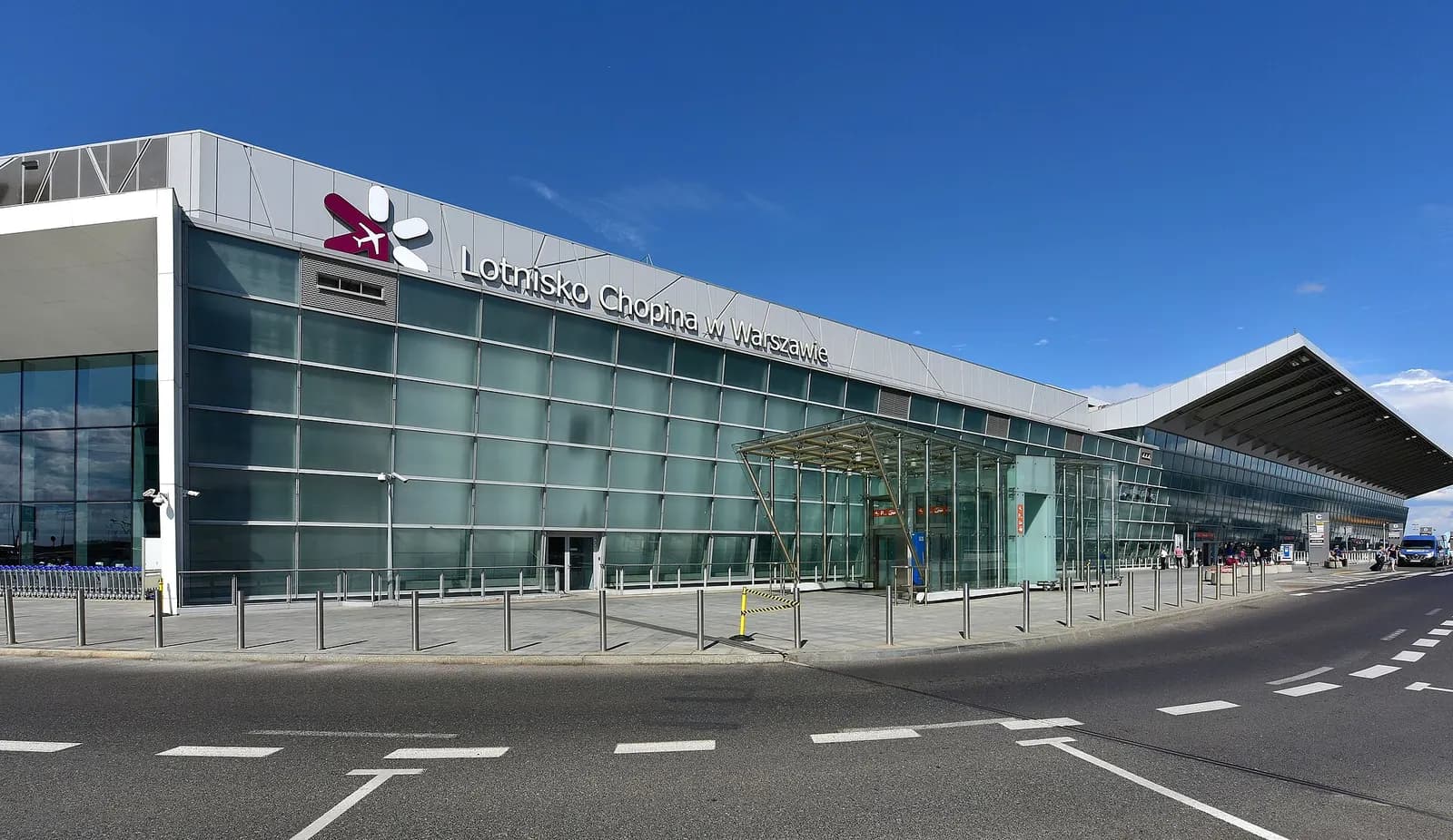 A panoramic exterior view of Warsaw Chopin Airport showing the terminal complex, control tower, and apron area.