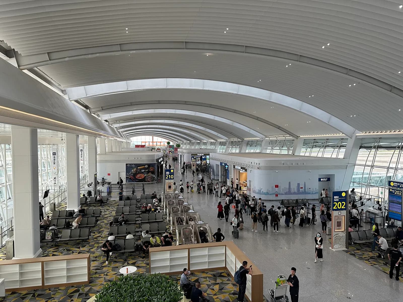 The departure concourse in Terminal 2 with gate seating areas, shopfronts, and large windows facing the airfield.