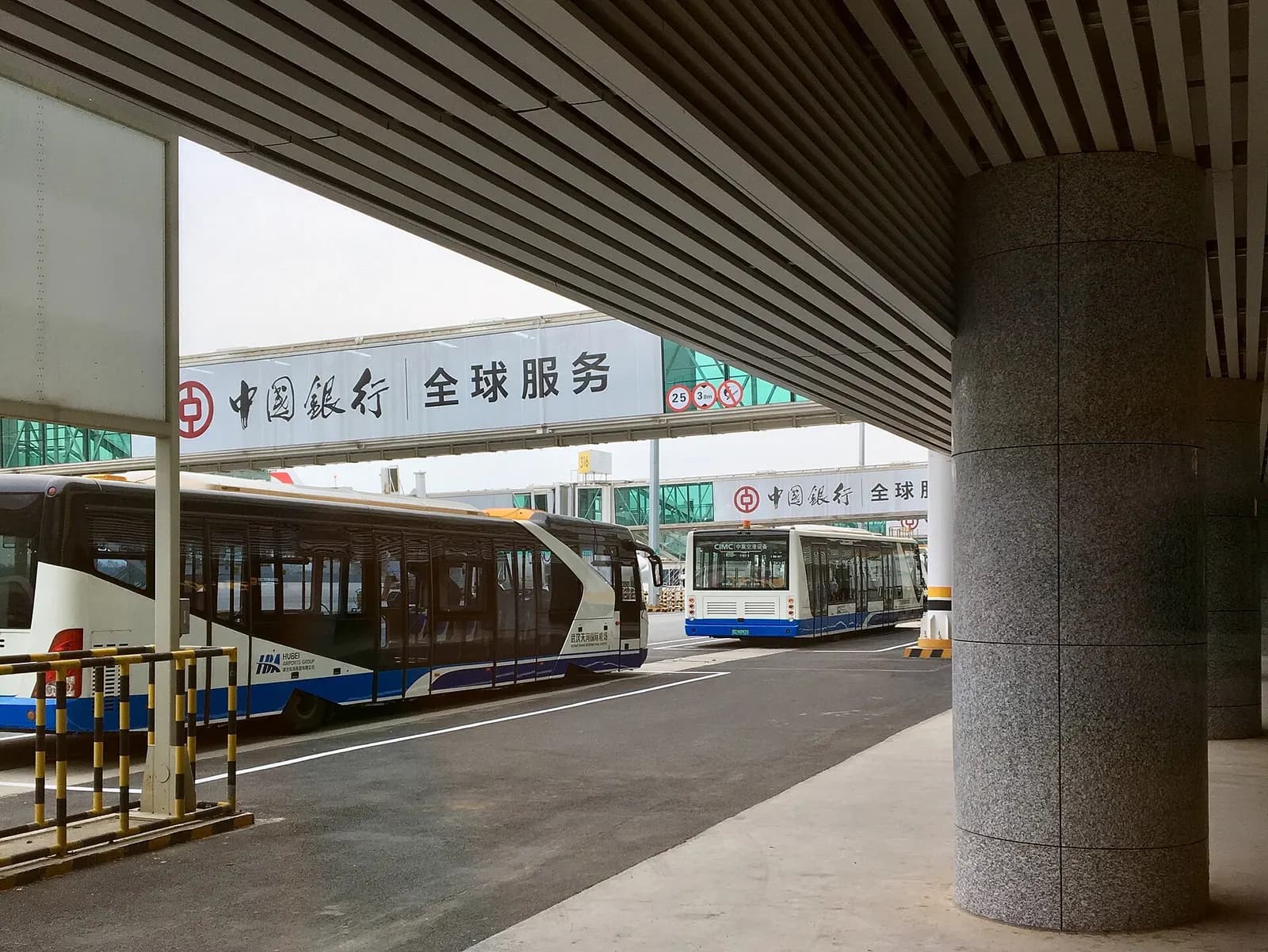 Several white airport shuttle buses lined up outside Terminal 3, used to ferry passengers to remote parking stands.