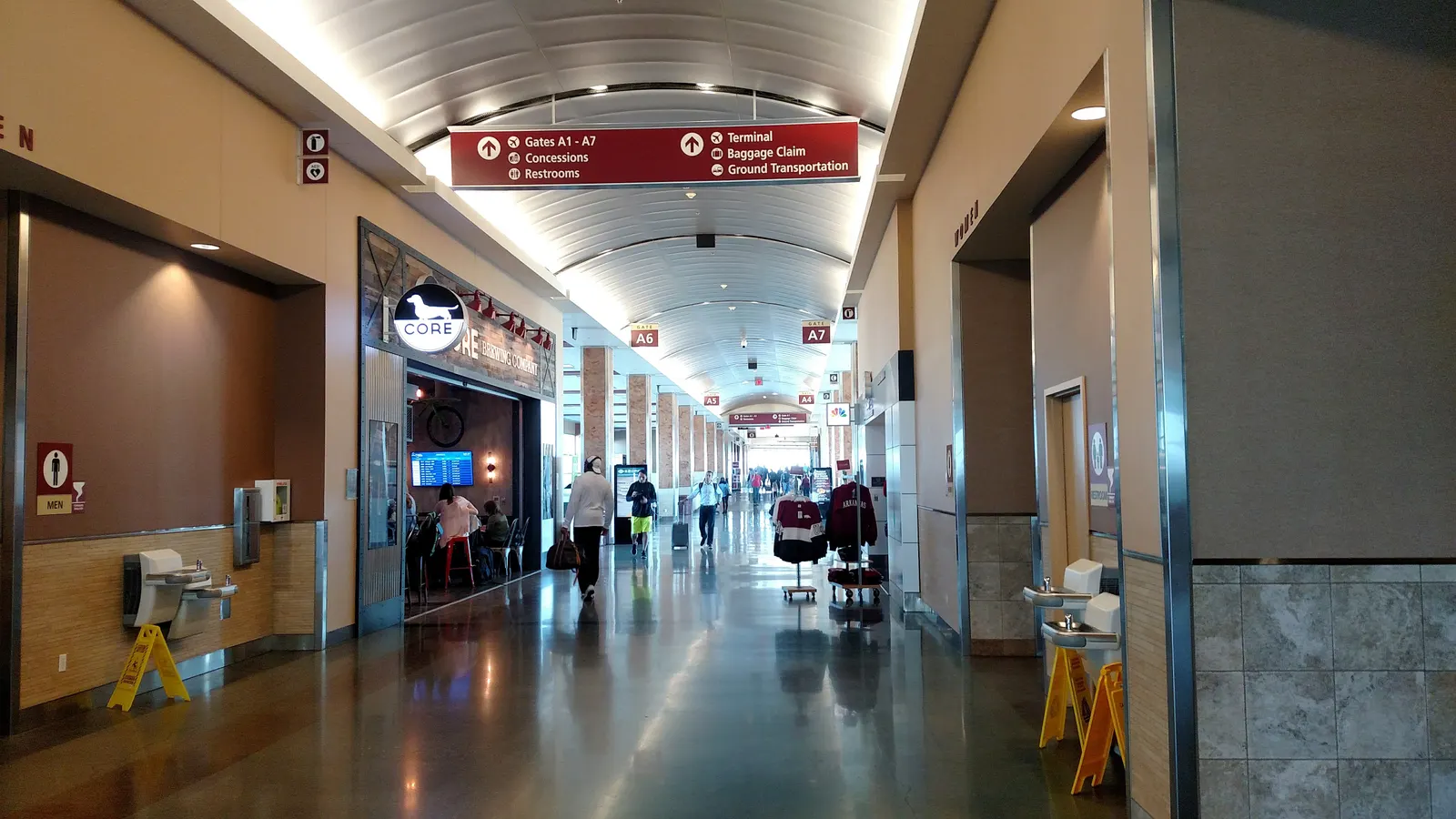 Concourse A at Northwest Arkansas National Airport looking toward Gates A5–A7, with a Core storefront on the left and drinking fountains on both walls.