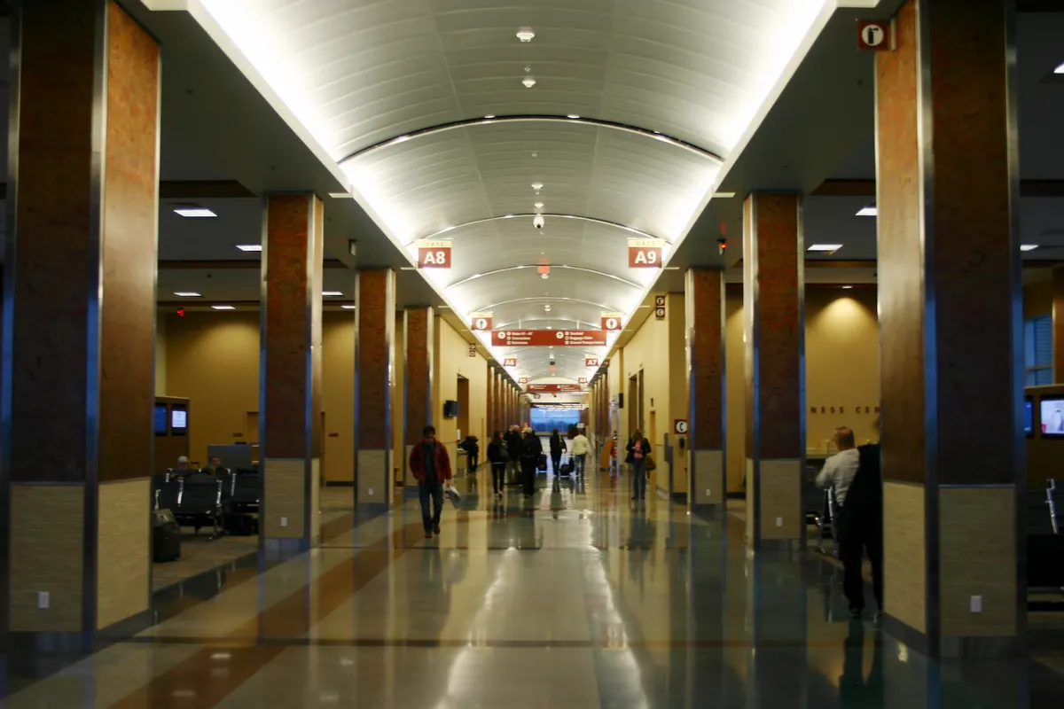 Long Concourse A hall at XNA with A8 and A9 column signs, a business-center doorway, and a few travelers on the terrazzo.