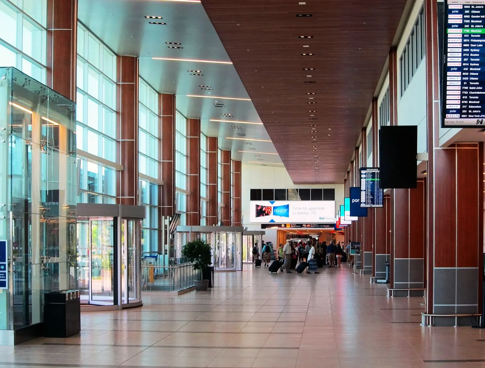 Landside hall at Halifax Stanfield with wood-clad columns, glass doors, and a bilingual departures board.