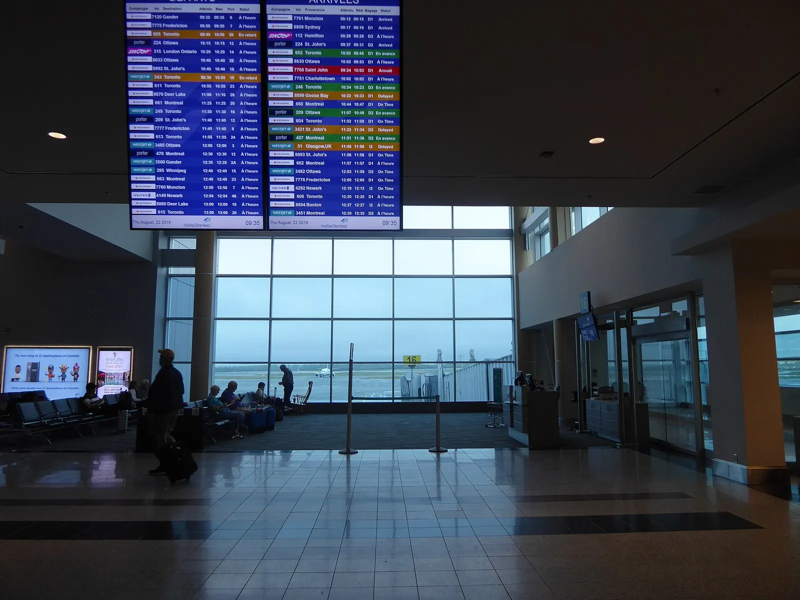 Airside holdroom FIDS screens reading Halifax Stanfield, with Gate 16 and a jetbridge visible beyond.