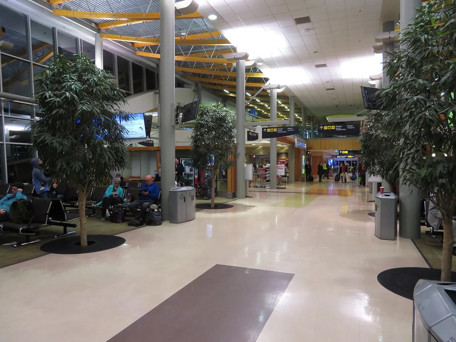 Airside corridor at Victoria International Airport with seating along the windows and retail ahead.