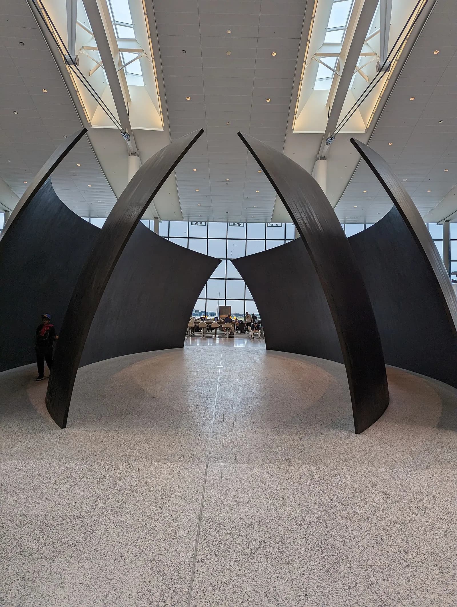 A large red suspended sculpture with interlocking circular forms hangs above the bright, open atrium of Terminal 1.