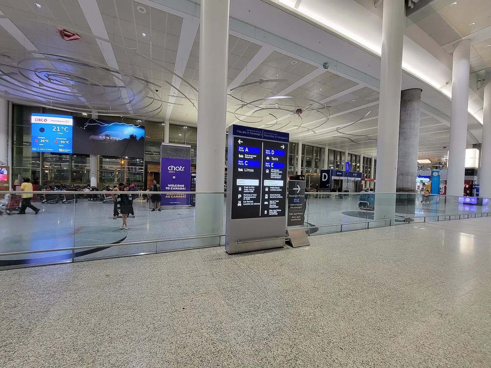 Travelers walk through the spacious, high-ceilinged international arrivals hall in Terminal 1 with directional signage overhead.