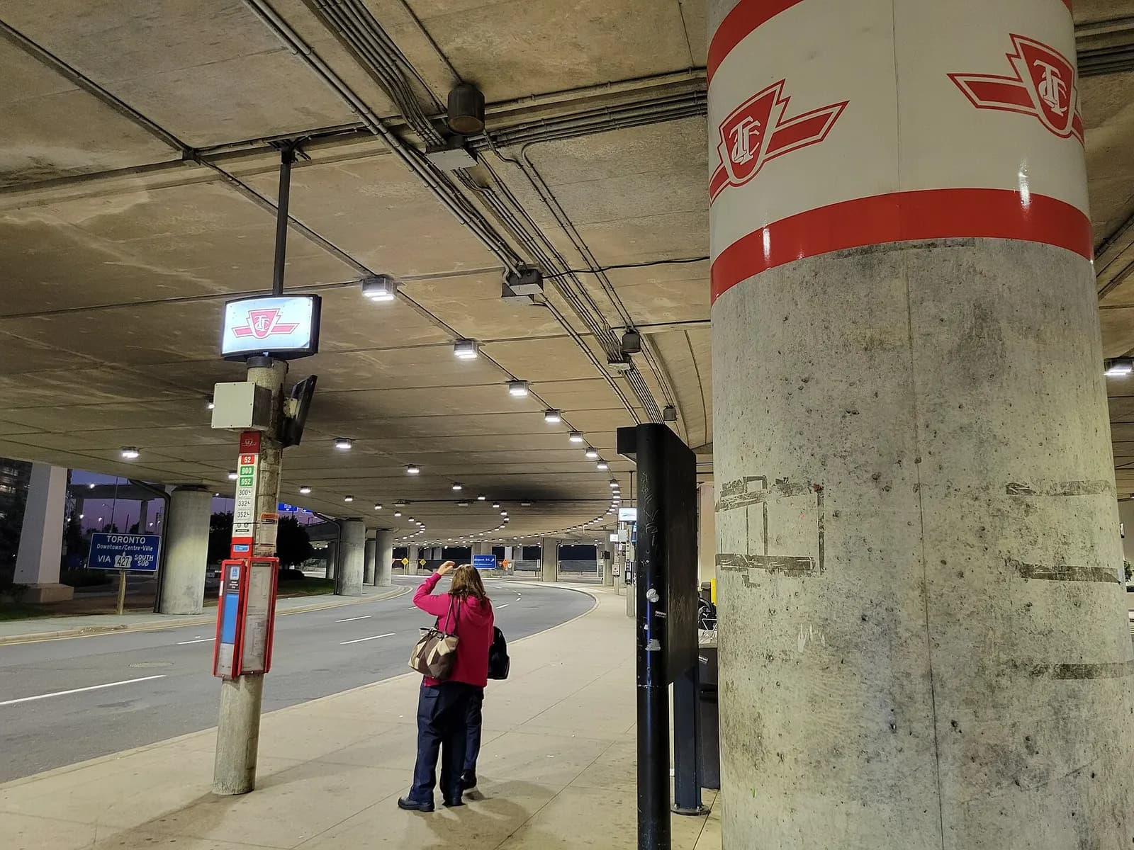 A TTC bus stop with route signage and shelter stands outside Terminal 1 for public transit connections.
