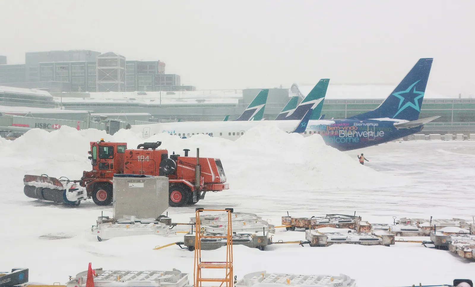 Snow covers the runways, taxiways, and terminal buildings of Toronto Pearson International Airport under a pale winter sky.