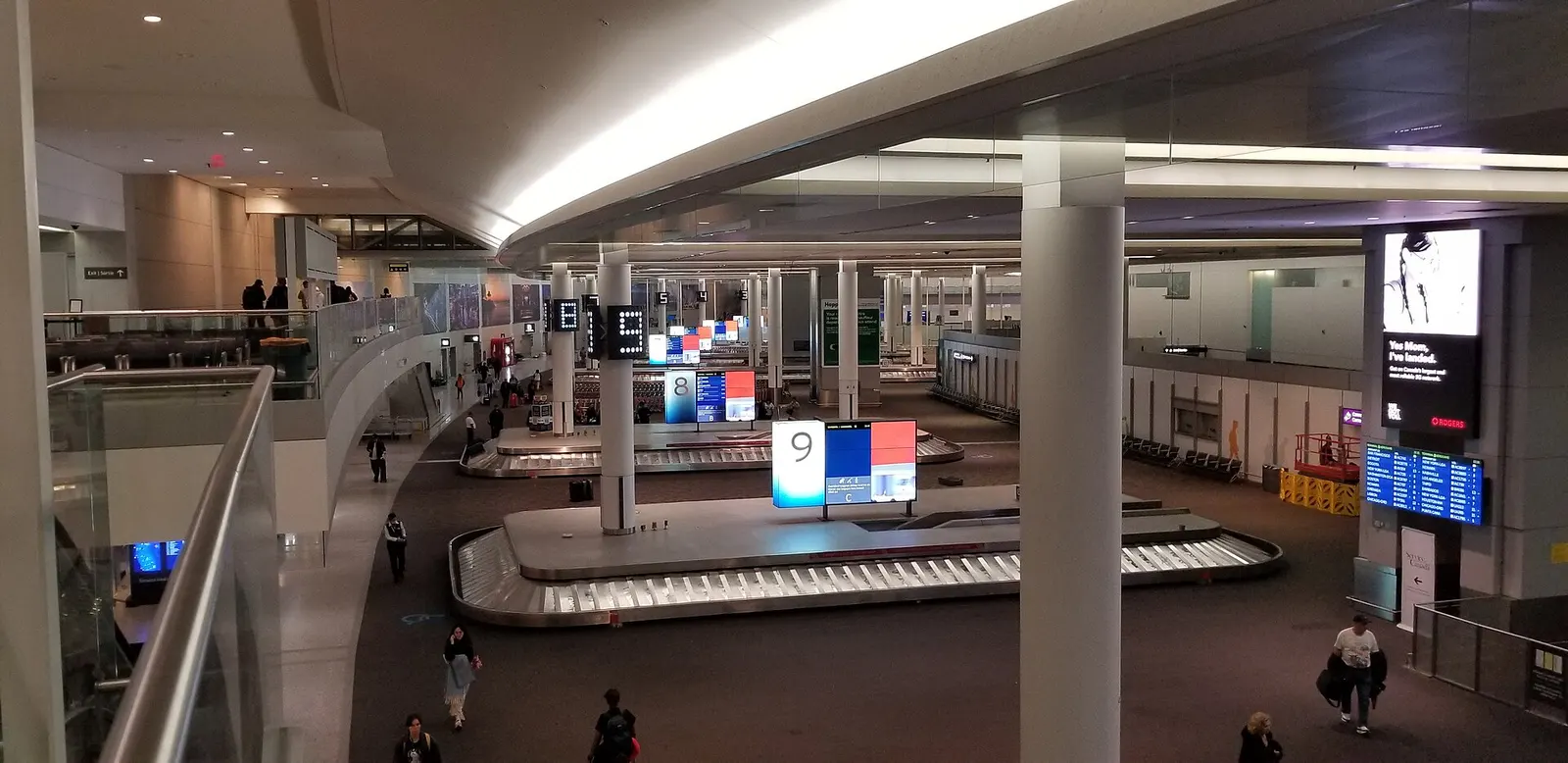 Several baggage carousels sit in a long, well-lit claims hall in Terminal 1 beneath overhead flight-information screens.