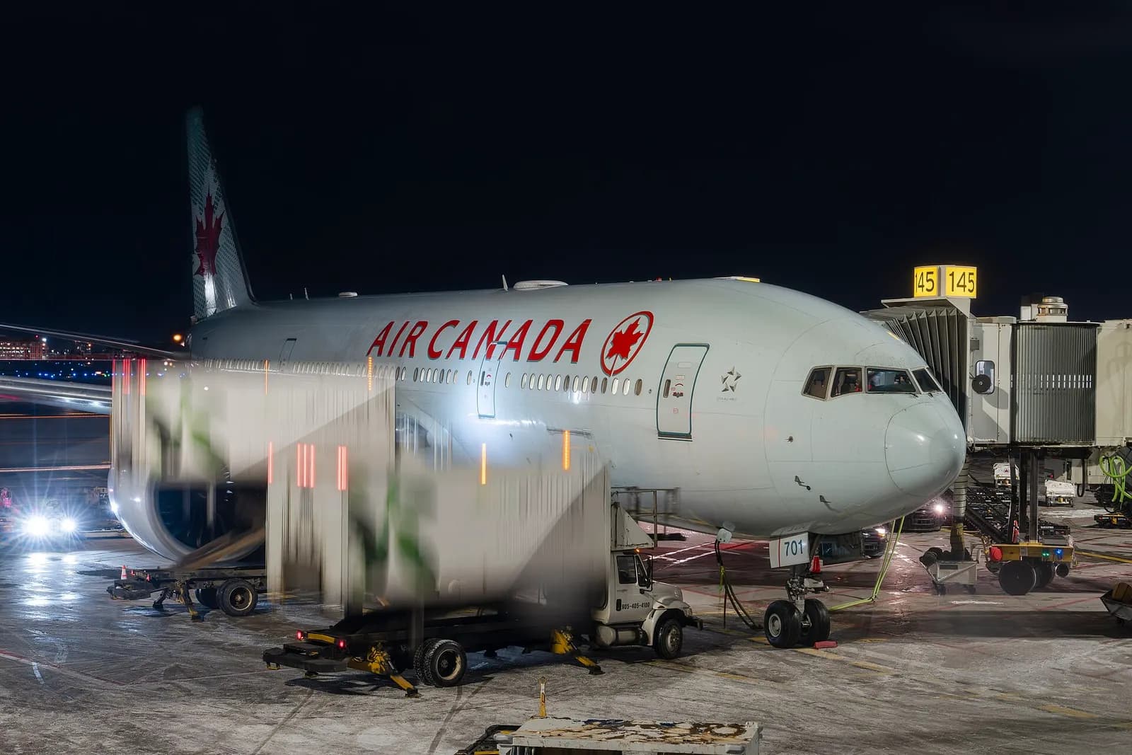 Air Canada Boeing 777-300ER (C-FIUA) at the gate at Toronto Pearson International Airport, with catering trucks positioning for loading.