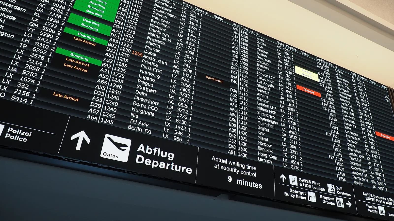 A large digital flight information board listing departure times, destinations, gates, and status updates in the terminal.