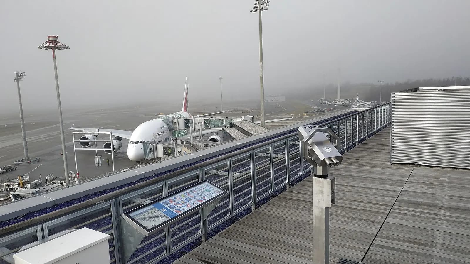 The public observation terrace at Dock E with glass railings overlooking parked aircraft, jet bridges, and the midfield apron.